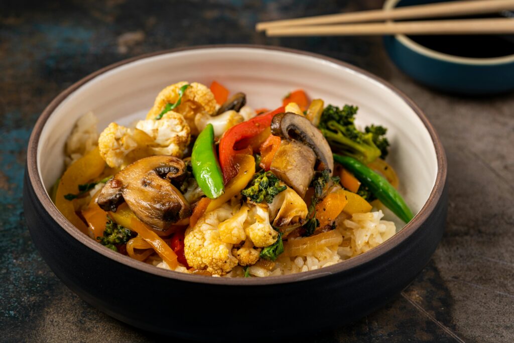 A vibrant bowl of vegetable stir-fry with rice, featuring mushrooms, broccoli, and bell peppers.