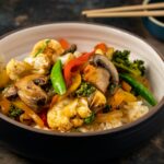 A vibrant bowl of vegetable stir-fry with rice, featuring mushrooms, broccoli, and bell peppers.